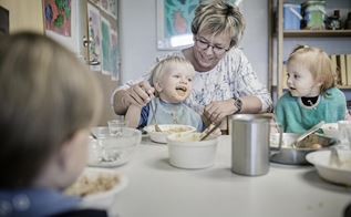 Pædagogisk assistent Helle Winkler sidder ved bordet sammen med tre mindre børn, der spiser frokost