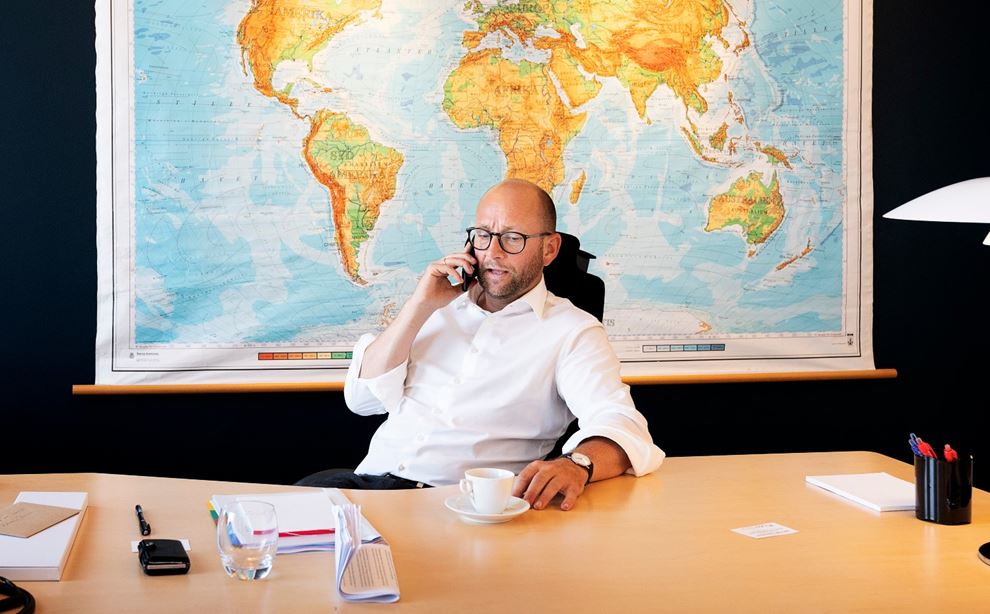 Rasmus Prehn sidder på sit kontor foran et stort verdenskort  og taler i telefon